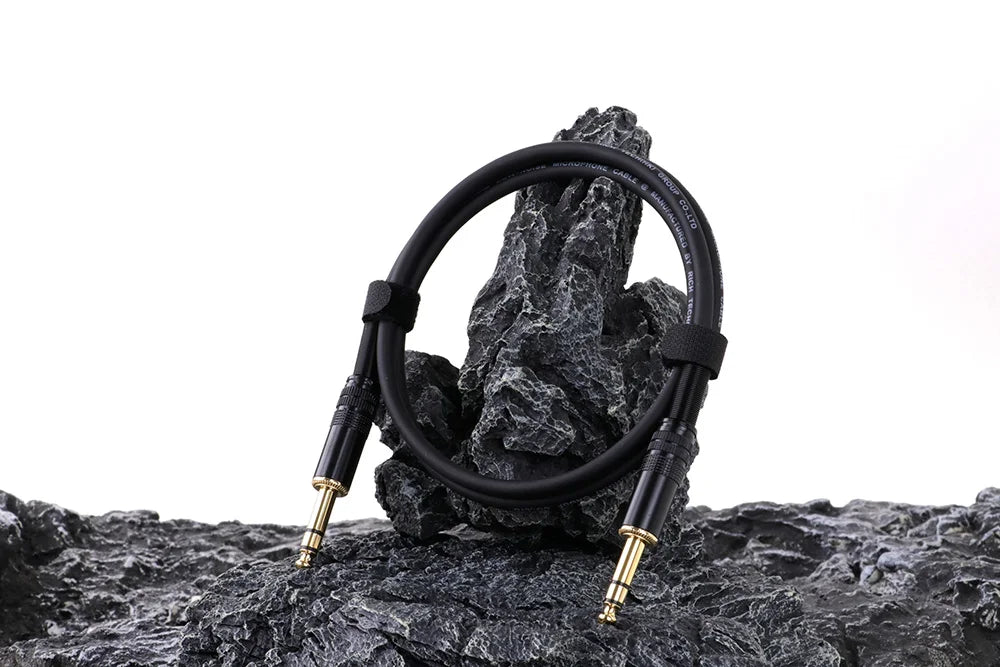 Black audio cable coiled on a rocky surface with a white background