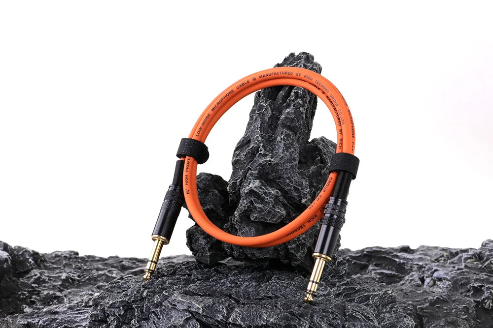 Orange audio cable coiled on a rocky surface with a white background